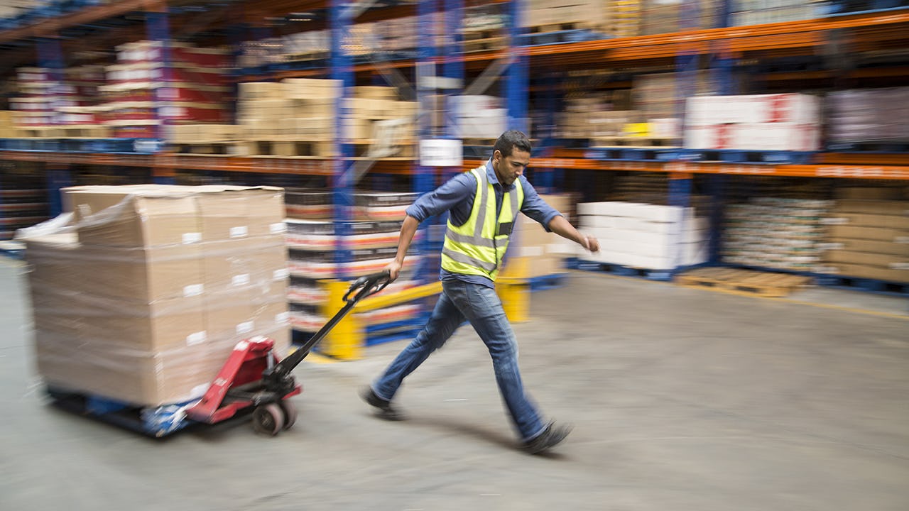 Worker pulling pallet truck inside a food distribution warehouse